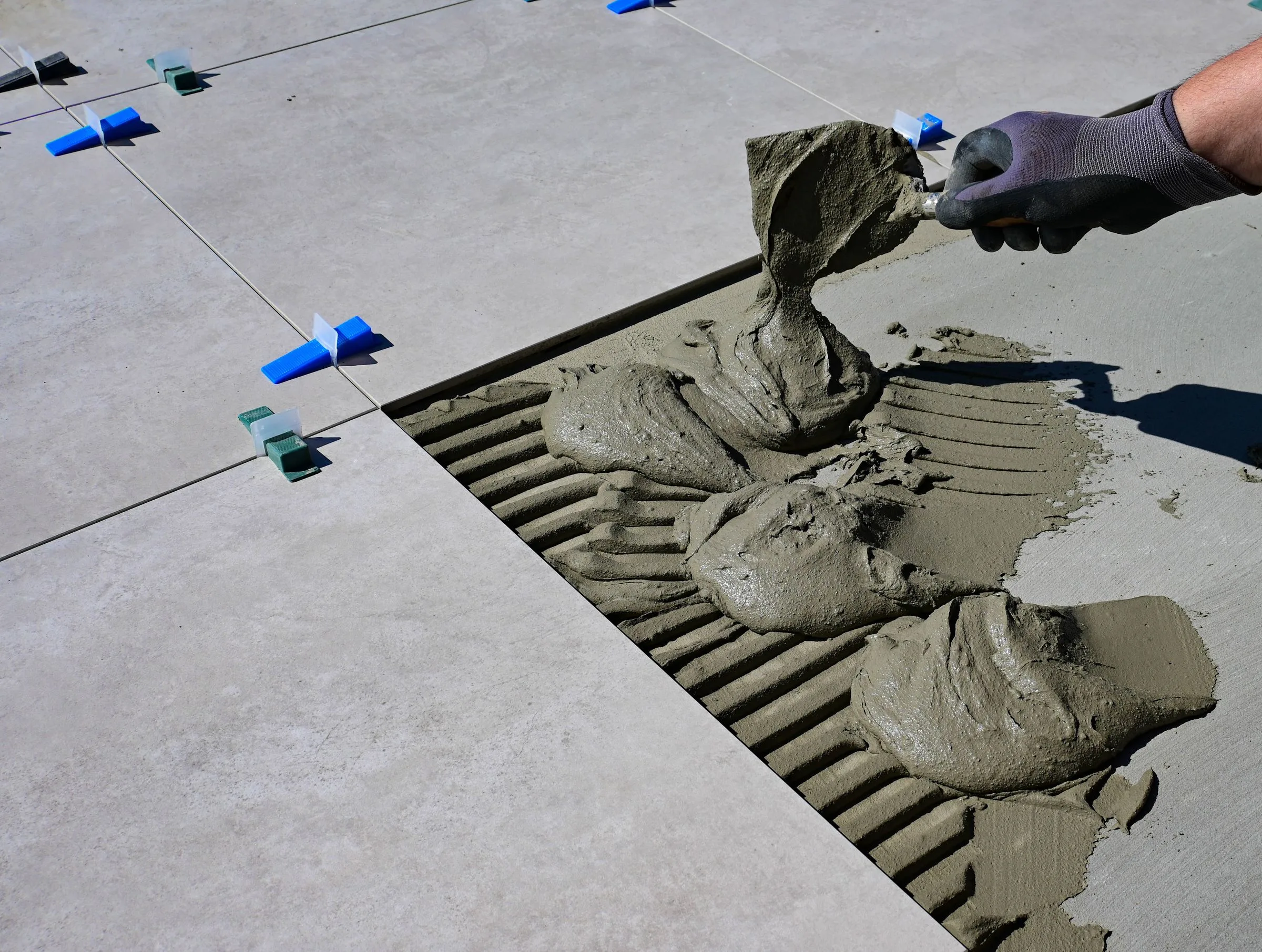 Illustrative gloved hand spreading mortar with a notched trowel